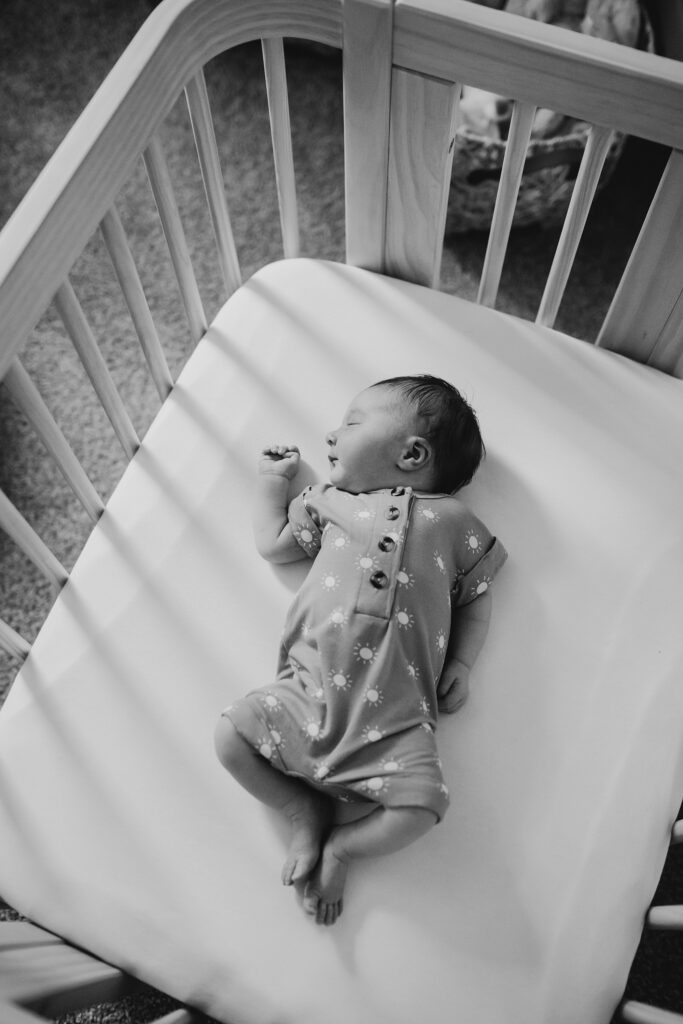 a black and white photo of a newborn baby asleep in his crib during a newborn photoshoot.