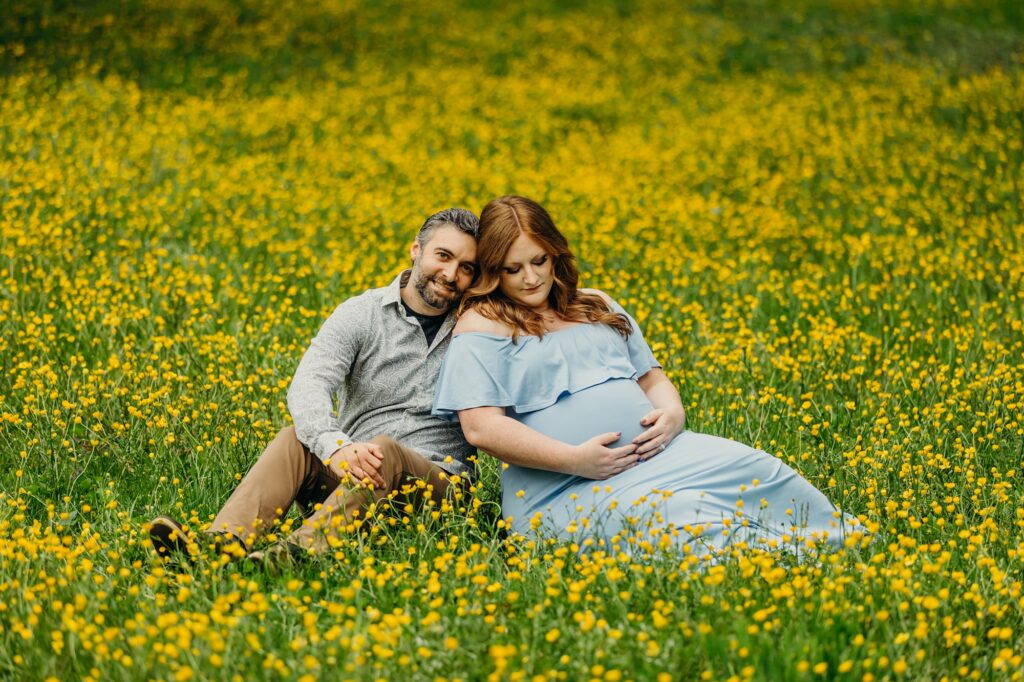 a couple posing in a blue maternity dress in a yellow flower field in Mt. Airy Philadelphia during their maternity photoshoot