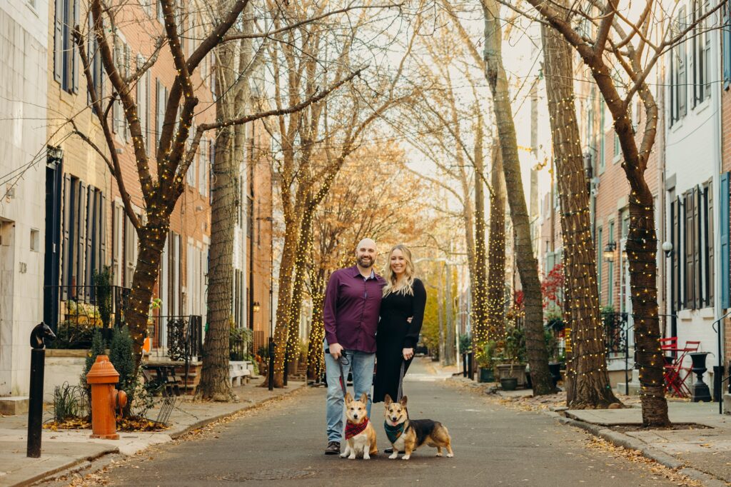 Philadelphia pet photoshoot for Christmas cards in Center City. a couple and their corgis surrounded by twinkling Christmas lights 