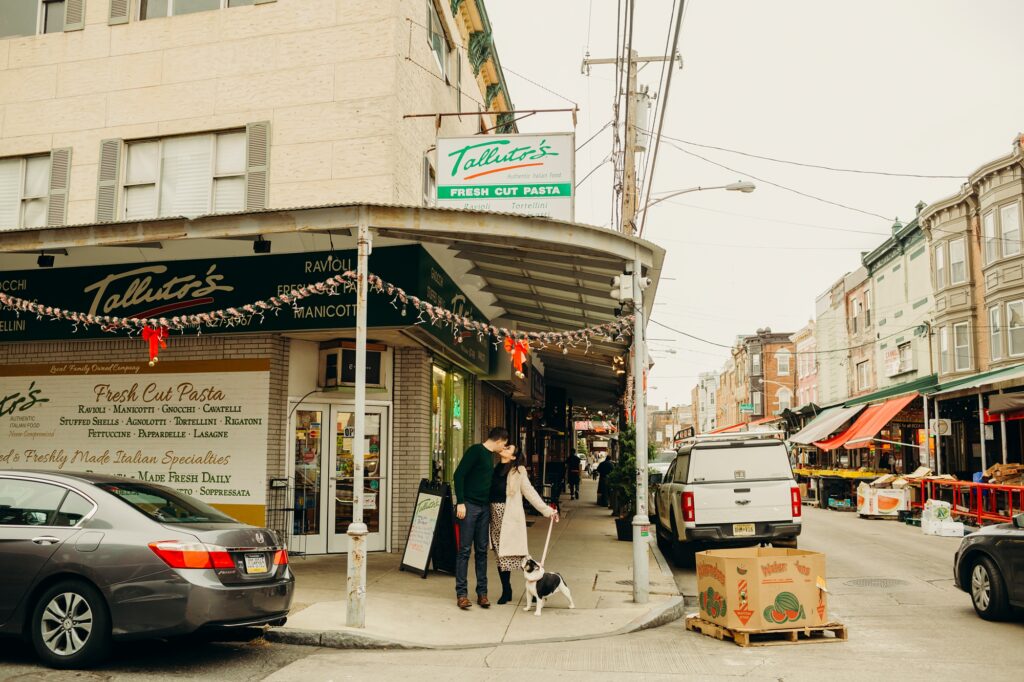 a couple in South Philadelphia with their bulldog standing in front of the Italian Market during the christmas season 