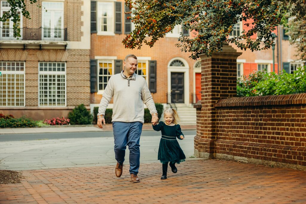 a little girl holding hands with her father as they walk near Rittenhouse Park in Center City Philadelphia during a lifestyle family shoot 