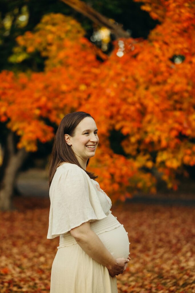Stunning portrait of a women in the peak fall season in New Jersey during her maternity session against orange leaves. 