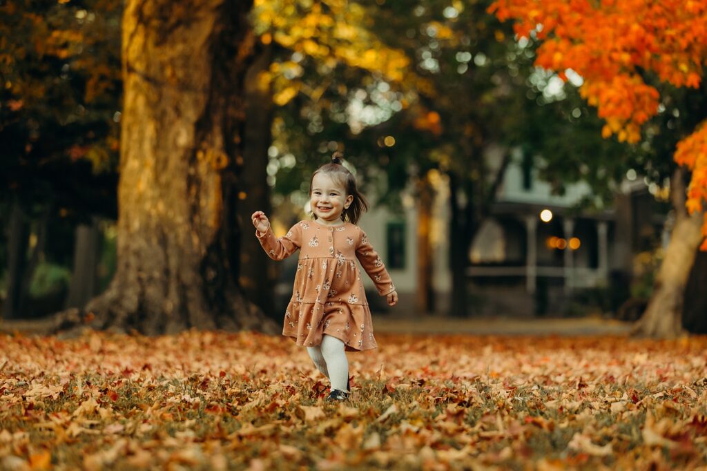 A little girl running through the leaves during a lifestyle family photoshoot in South Jersey during the peak fall season. 